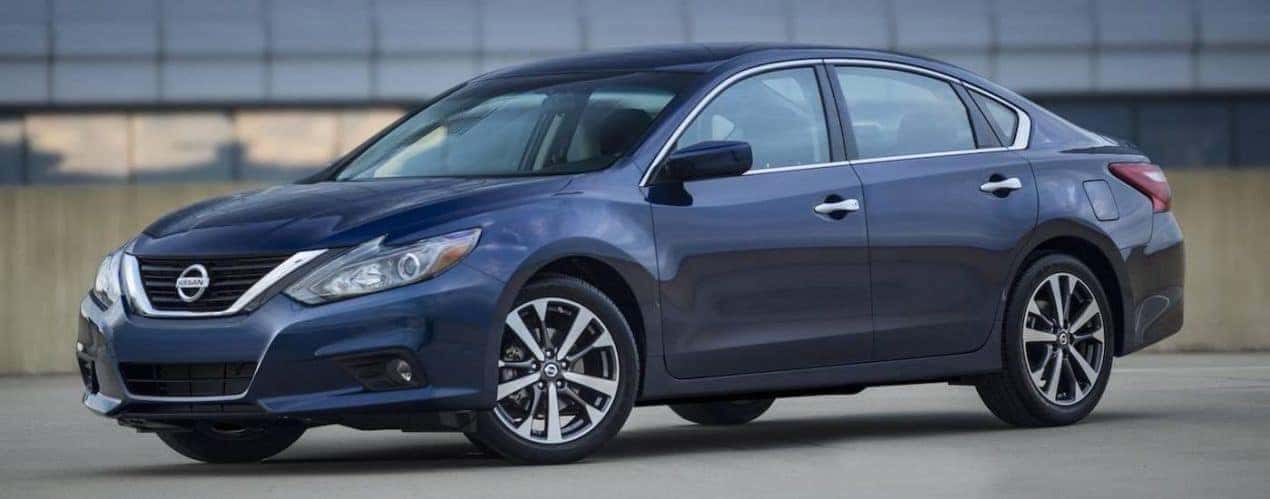 A dark blue 2016 used Nissan Altima is shown in front of a glass building.