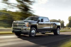 A black 2015 Chevy Silverado 3500HD with dual rear wheels is driving on a rural highway.