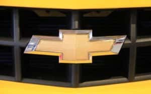 The closeup is shown of a gold Chevy bowtie emblem on a yellow Camaro.