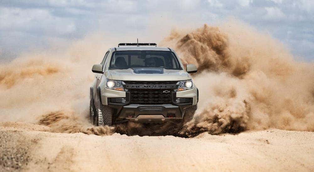 A tan 2021 Chevy Colorado ZR2 is kicking up sand and shown from the front.