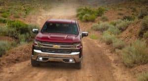 A popular Chevy truck for sale, a red 2020 Chevy Silverado 1500, is shown from the front driving on a dirt road.