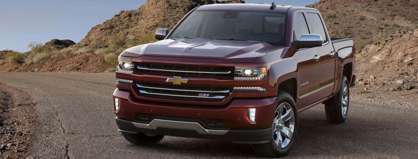 A dark red 2018 Chevy Silverado is parked on a paved road with dirt hills in the background.