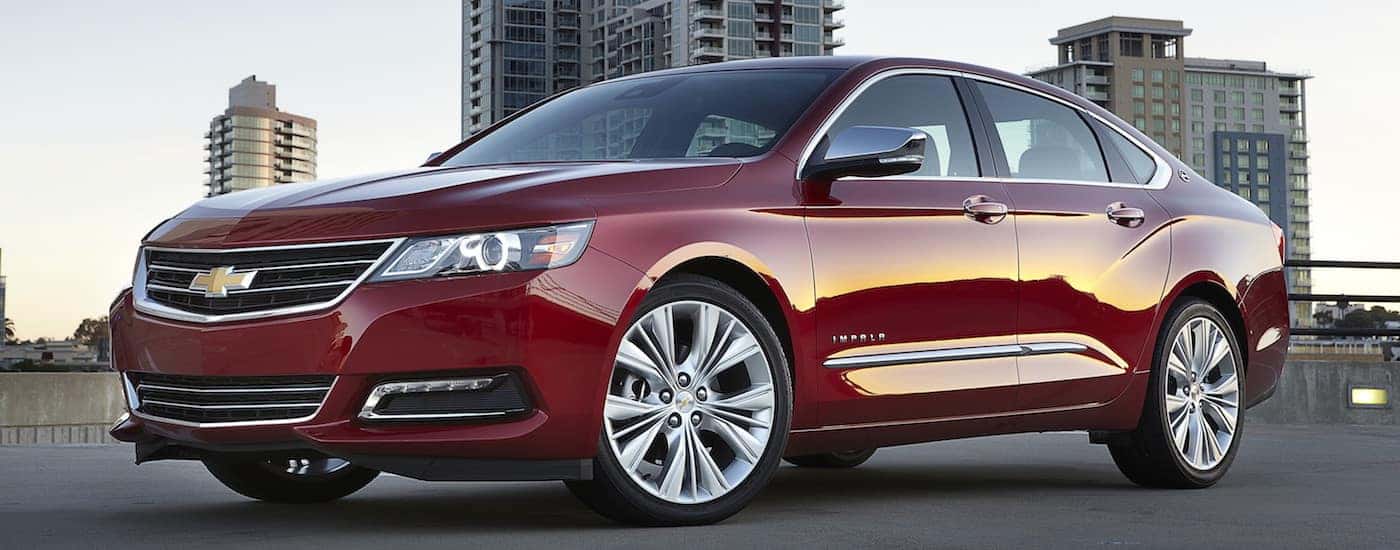 A red 2018 Chevy Impala parked in a parking low with city buildings in the background.