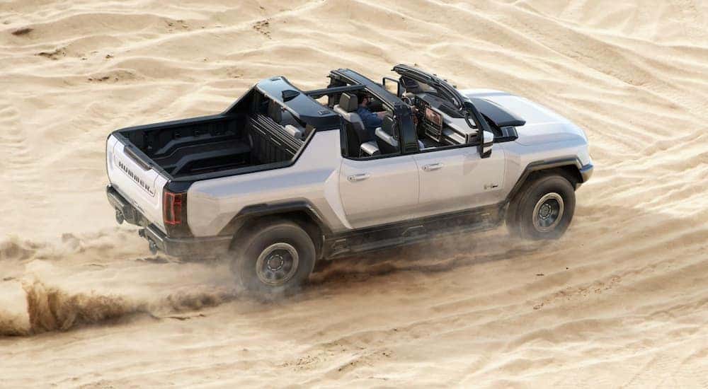 A silver 2022 GMC Hummer EV is shown off-roading in a desert after looking at Chevy cars. 