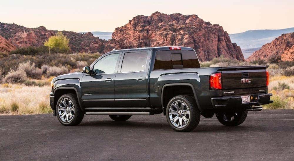 A dark grey 2018 GMC Sierra 1500 is shwon from the rear in front of desert mountains.