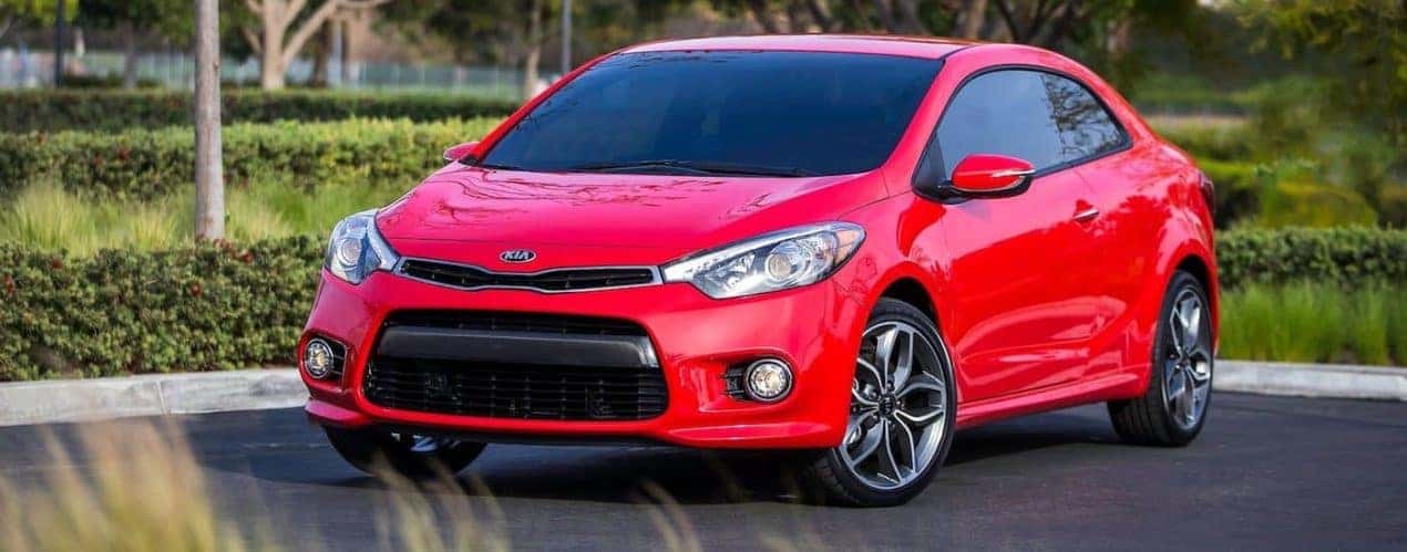 A red 2014 used Kia Forte is parked in front of hedges.