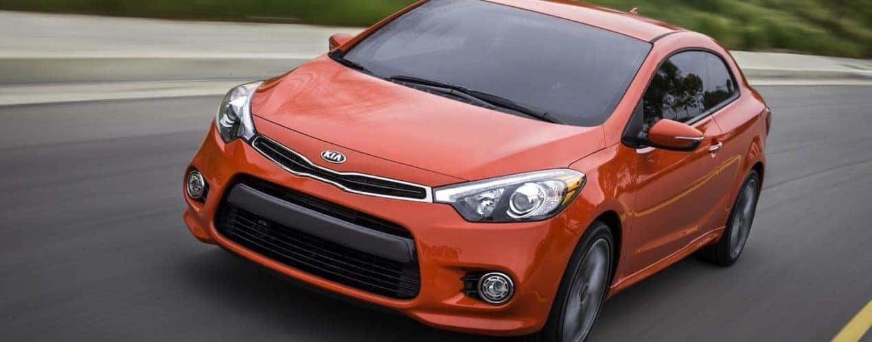 An orange 2015 used Kia Forte is shown driving on highway.