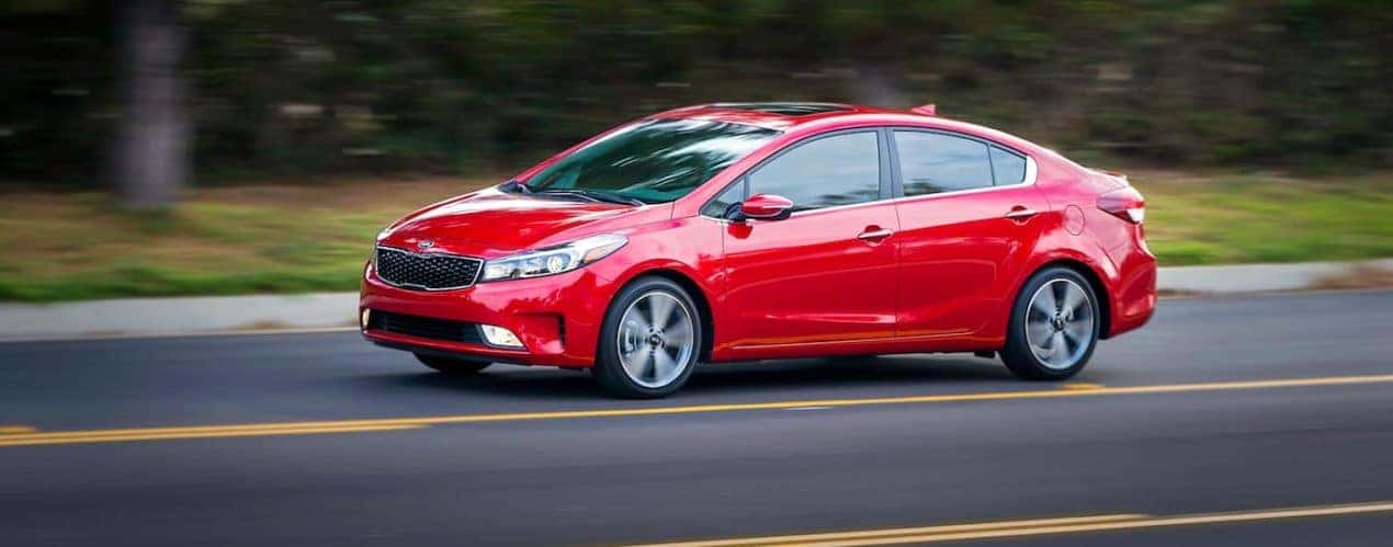 A red 2017 used Kia Forte EX is driving on a country highway.