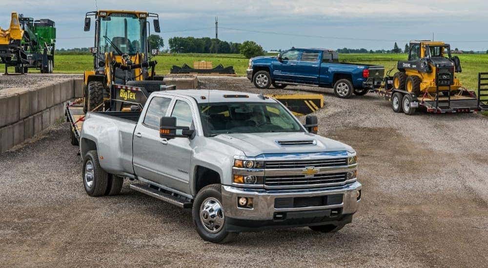 A white 2018 Chevy Silverado 3500HD is parked with other trucks and trailers with construction equipment.
