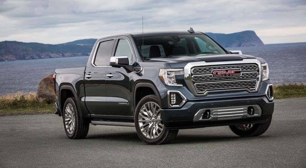 A gray/blue 2020 GMC Sierra Denali is parked in front of a lake and mountains.
