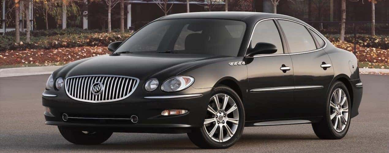 A black 2009 used Buick LaCrosse in a parking lot with trees and buildings in distance.