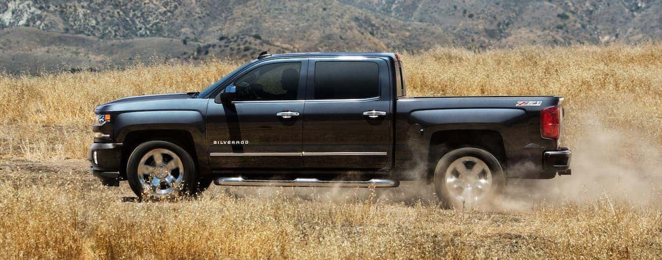 A black 2018 Chevrolet Silverado is driving on a dirt road through a field after winning the 2018 Chevrolet Silverado vs 2018 Ram 1500 comparison.