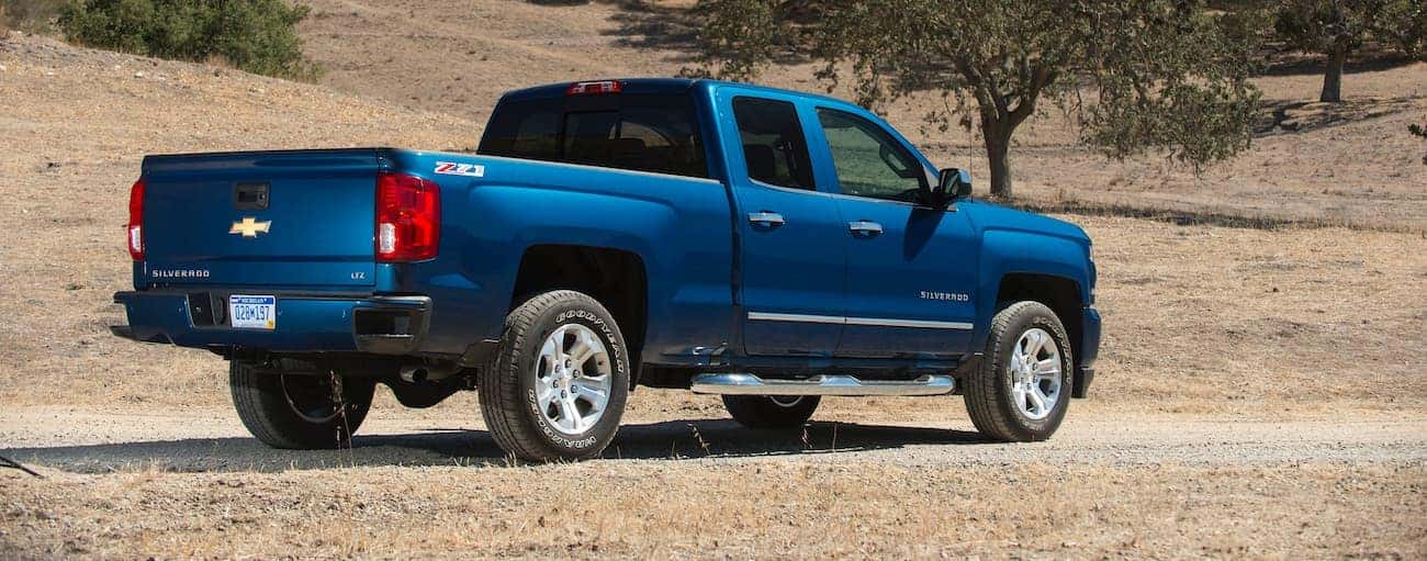 A blue 2018 Chevrolet Silverado is shown from the rear on a dirt road.