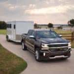 A black 2016 Chevy Silverado 1500 is towing an enclosed trailer on a farm driveway.