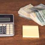 Cash and a grey calculator are shown on a desk at a buy here pay here dealership in Indianapolis.