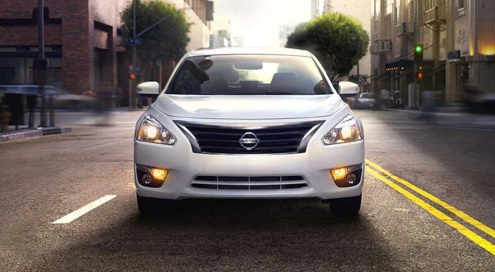 A white 2014 Nissan Altima is shown from the front driving on a city street.