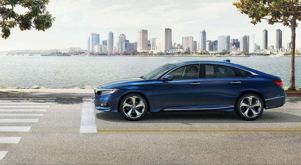A blue 2020 Honda Accord is shown from the side driving on a road next to a body of water.