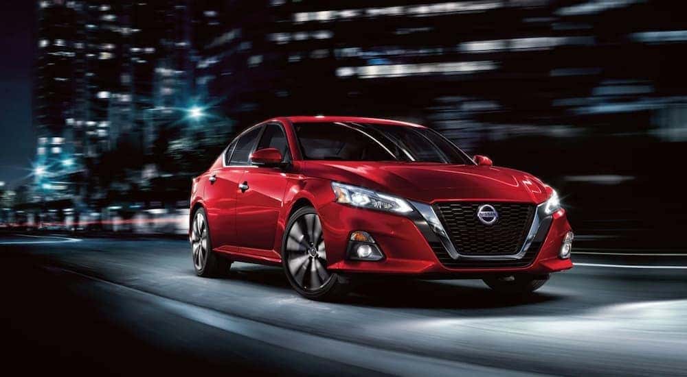 A red 2020 Nissan Altima is shown driving through a city at night.