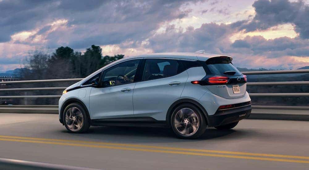 A popular used car in Cincinnati, a blue 2022 Chevy Bolt EV, is shown from the side driving over a bridge.