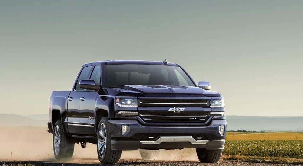 A black 2016 Chevy Silverado 1500 Z71 with a truck bed liner is shown driving on a dusty dirt road.