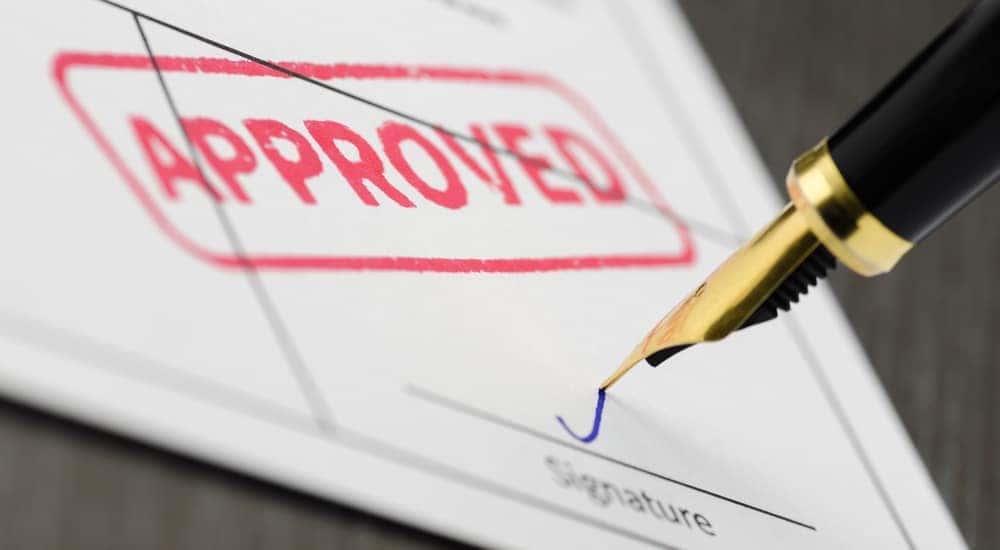 A fountain pen is shown signing a document at a buy here pay her dealership.