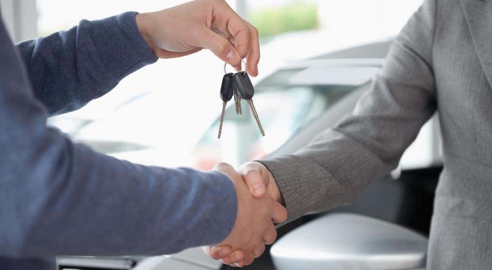 People shaking each other hands while holding car keys are shown.