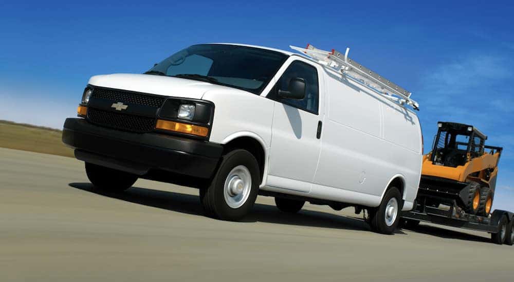 A white chevy van pulling a utility trailer