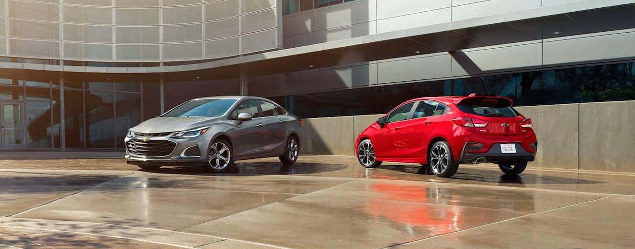 Gray 2019 Chevy Cruze sedan and red hatchback in front of office building