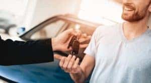 A dealer's hand is giving keys to a smiling man at a Buy Here Pay Here Louisville.