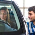 Young woman, behind the wheel of a second hand car, being assisted by a man