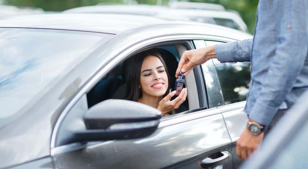 A person is shown sitting in the drivers seat of a car as a salesperson passes a key.