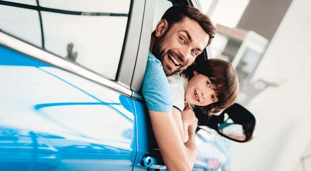 Man and child are shown leaning out of blue car.
