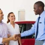 Couple shaking hands of car salesman, red car in back
