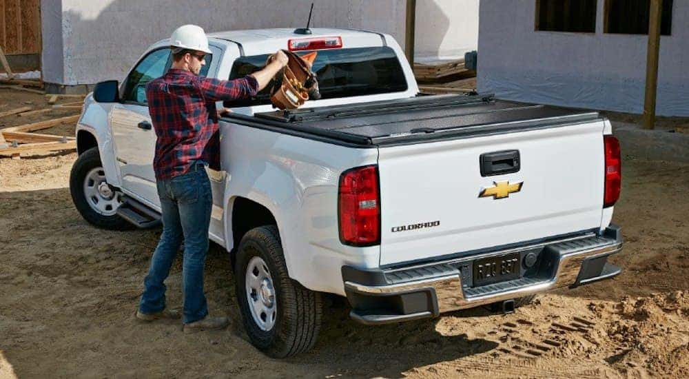 A worker loads a tool belt into the back of a white 2018 Chevy Colorado with a tonneau cover