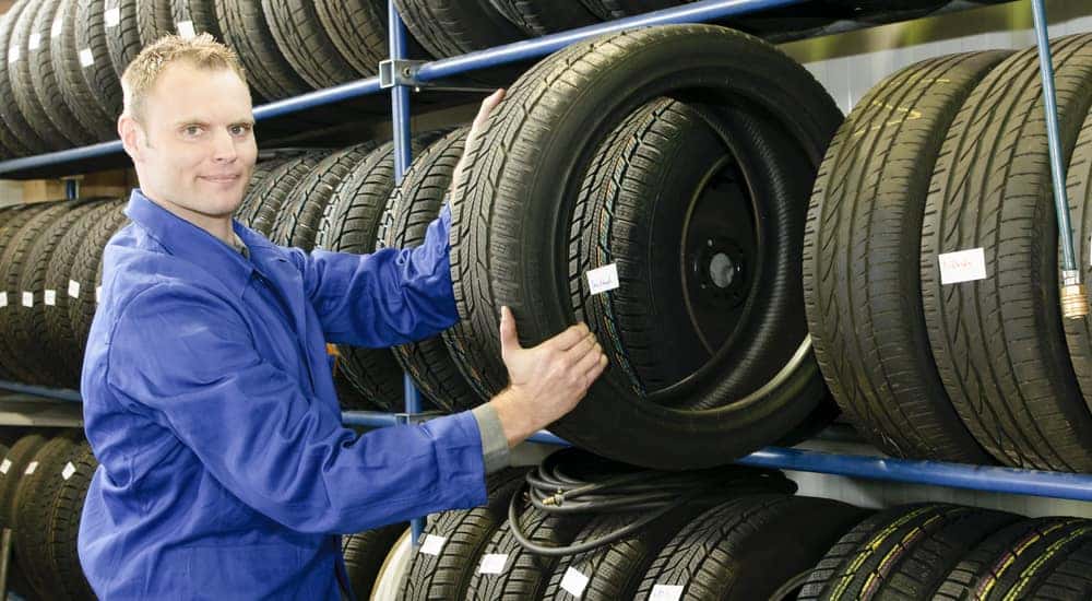 A man in a blue uniform pulls a tire from a tire rack at a tire shop