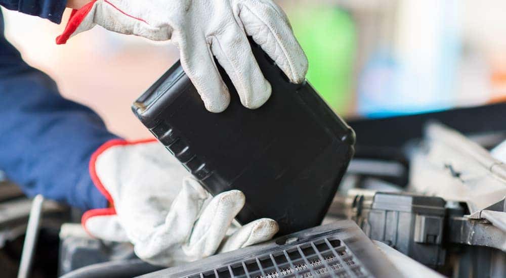 A mechanic wearing gloves pours oil into a car