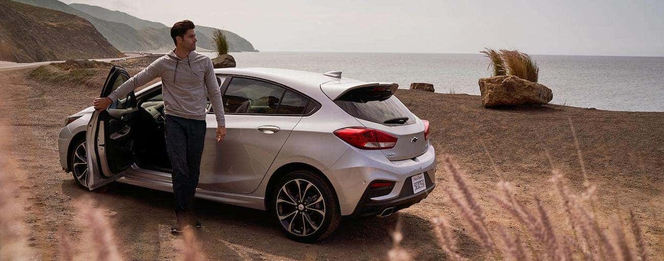 A man steps out of a silver 2019 Chevrolet Cruze hatchback at a beach