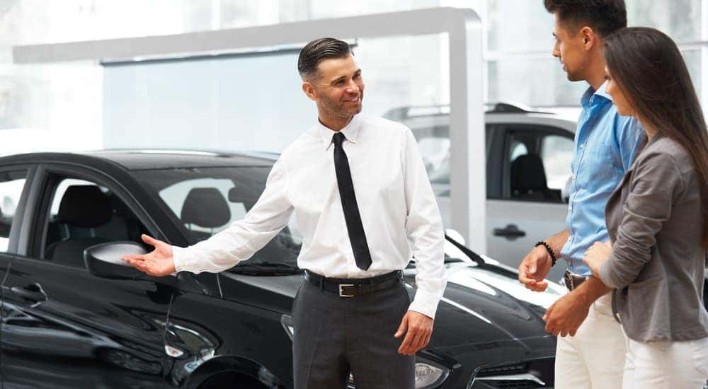 A car salesman is showing a couple looking at various buy here pay here cars.