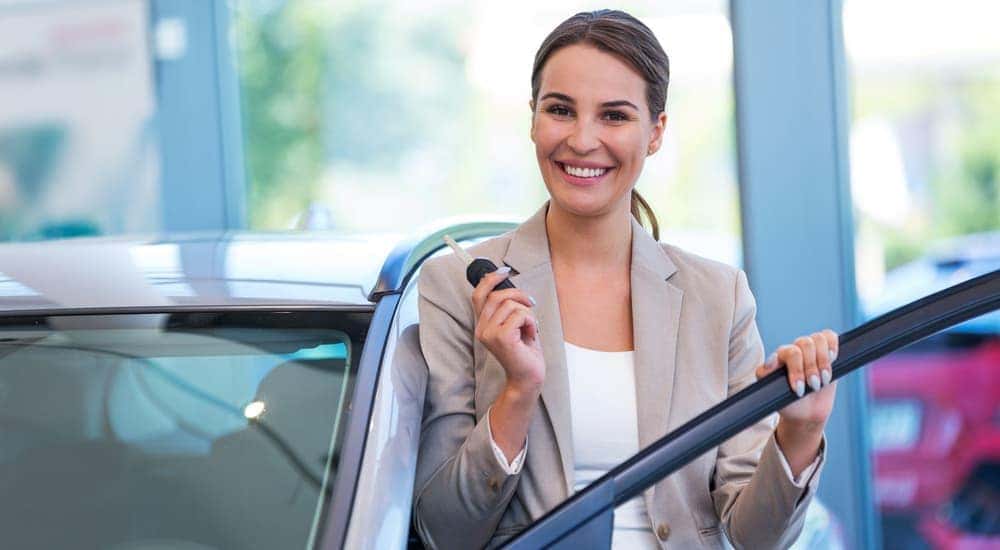 A woman stands inside a dealership with her new car key.