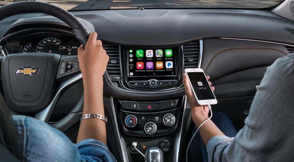 An iPhone is charging with an added cable, one of many great car accessories, while two women drive through Cincinnati, OH in their Chevy.