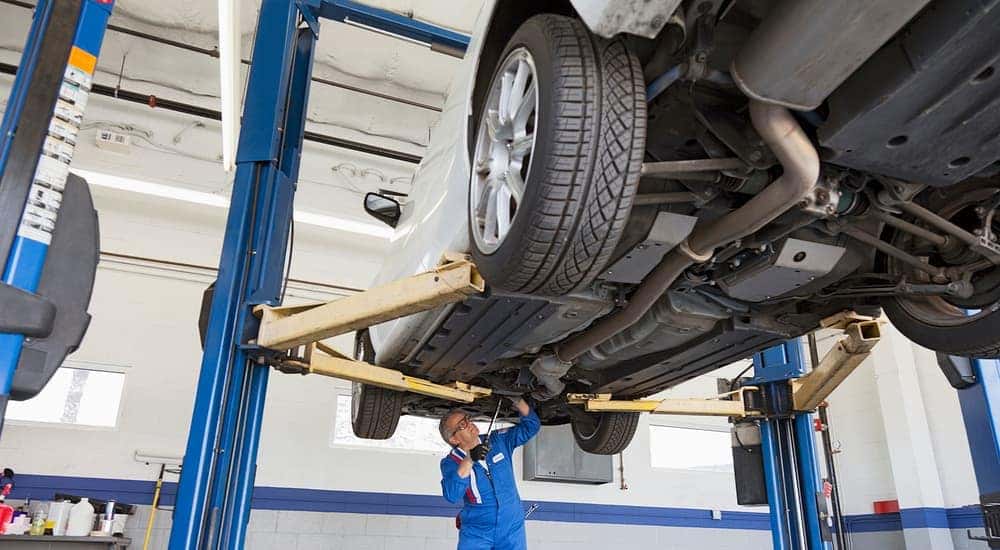 A mechanic is shown working from underneath a car on a lift.