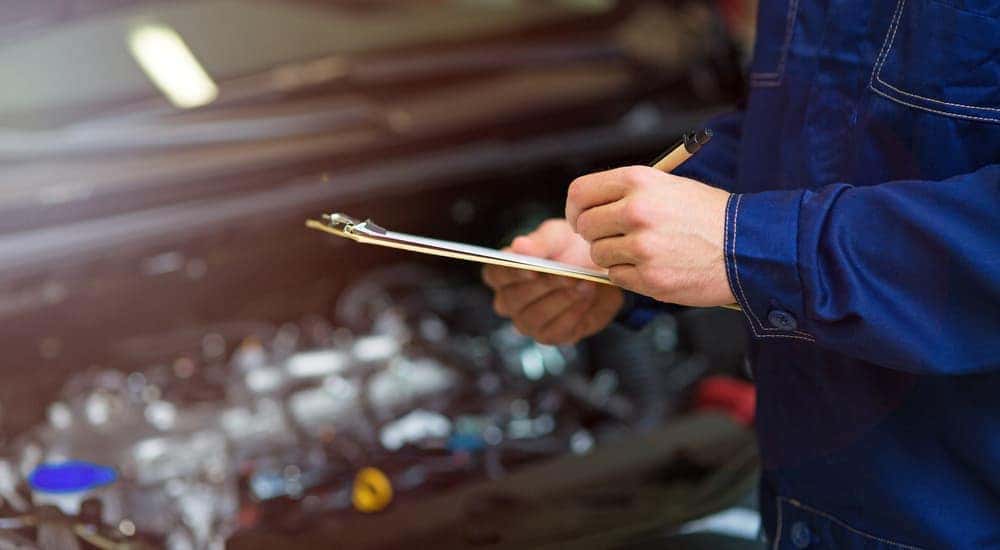 A close up of a mechanic holding a clipboard with a motor out of focus behind him. When searching for "quick oil change near me" a trusted dealership will show up.