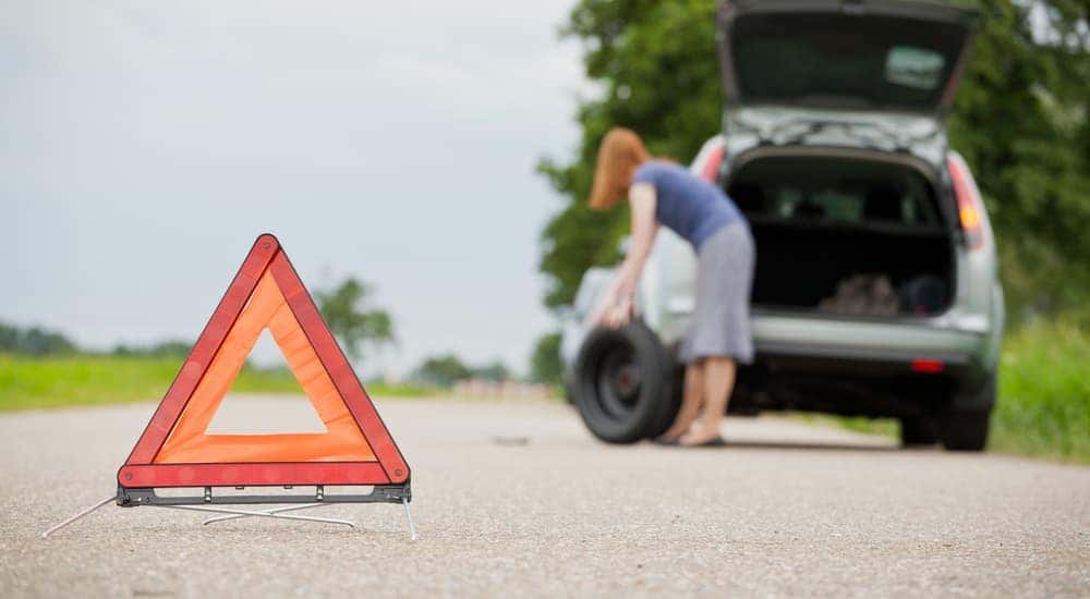 A woman is taking a spare tire out of her trunk in the background of a hazard sign after one of her tires in Cincinnati blew.