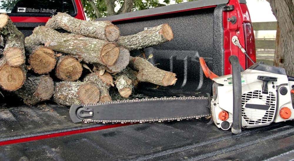 Logs and a chainsaw are sitting in a truck bed lined with Hardline. Hardline is the heavy duty option for Rhino's truck bed liners.