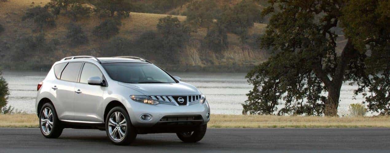 A silver 2009 used Nissan Murano is parked in front of a pond.