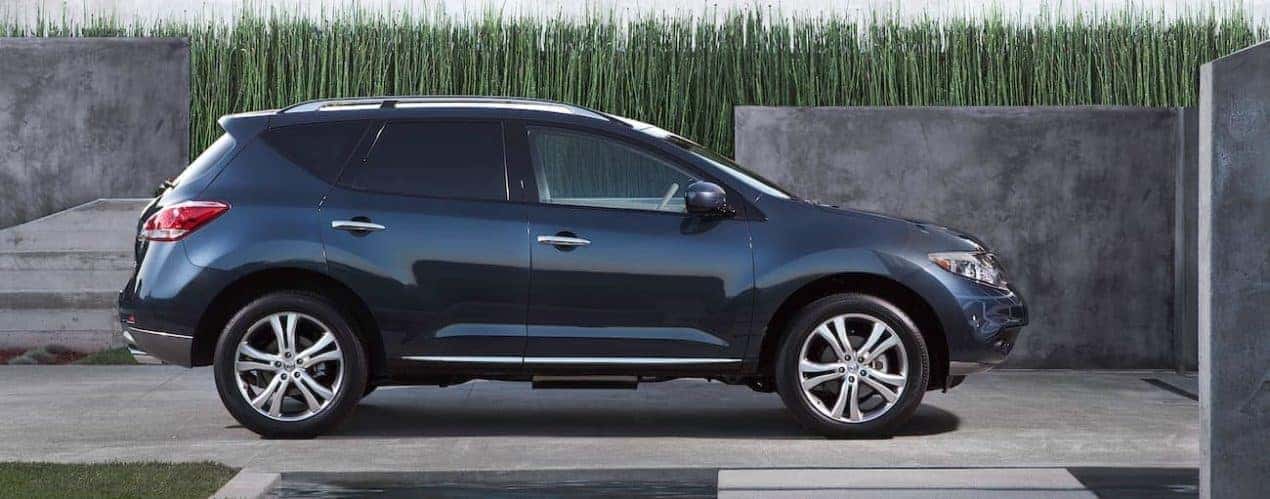 A dark blue 2011 used Nissan Murano is parked in a driveway with tall grass.