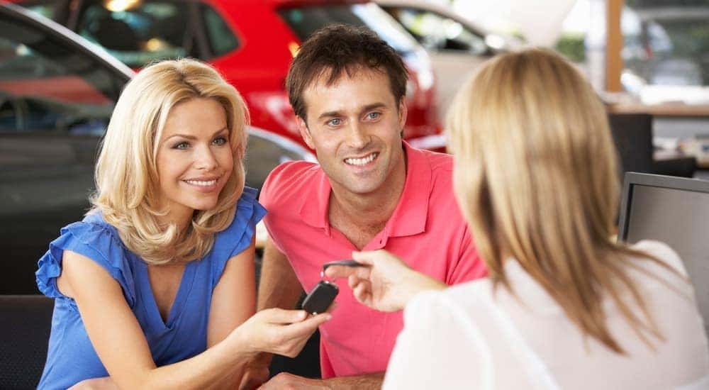 A saleswoman is handing a couple the keys to their new car at a buy here, pay here dealership in Cincinnati, OH.