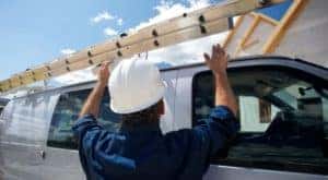 A construction worker is putting a ladder on the top of his white 2019 Chevy Cargo van, one of the popular Chevy vans for sale in Cincinnati, OH.