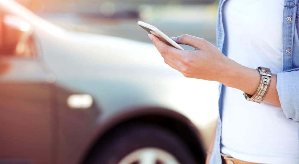 A car is out of focus while a woman's handing are holding her phone as she searches for her car's trade in value in Cincinnati, OH.