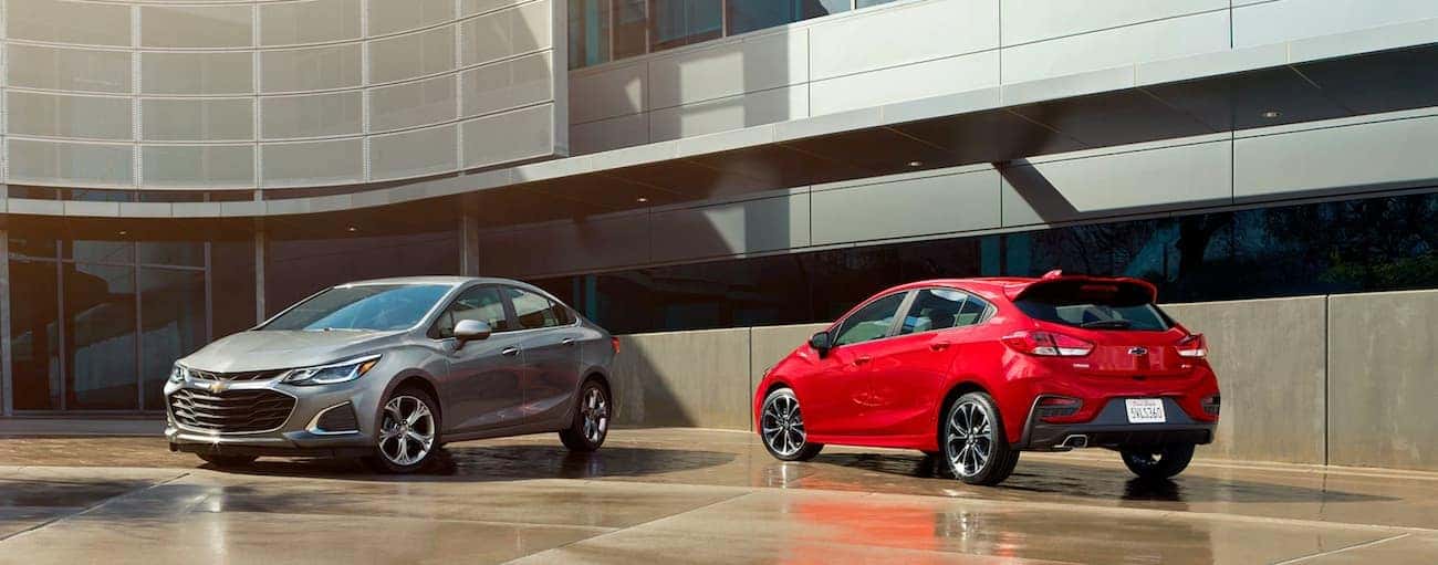 A grey 2019 Chevy Cruze is parked next to a red 2019 hatchback outside a glass building near Cincinnati, OH.